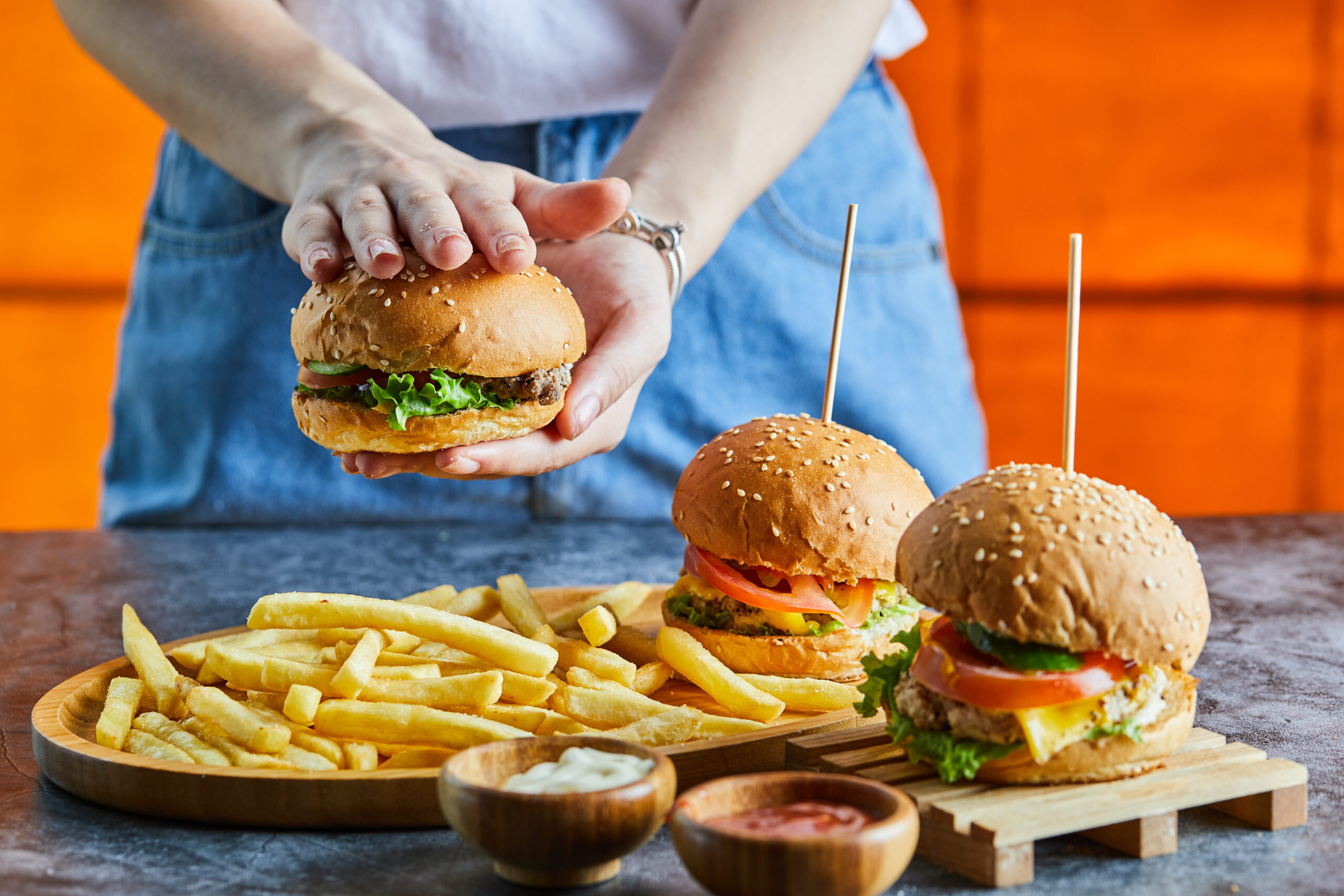 žena pripravujúca nezdravé jedlo A woman hand holding cheeseburger with fry potato, ketchup, mayonnaise . High quality photo